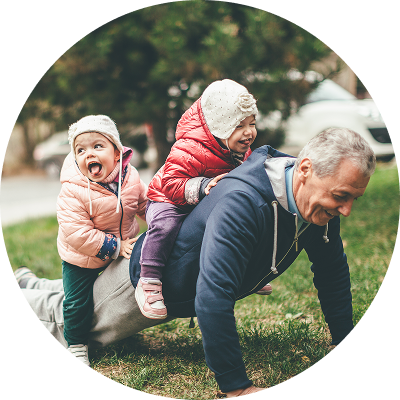 A grandfather doing a push-up with two small children laughing on his back, symbolizing strength and legacy; conceptually tied to the idea of protecting family wealth through an irrevocable trust.