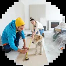 Young couple and their dog working together on a home remodel, measuring and cutting drywall with tools, preparing to install plasterboard—consider using a Civic HELOC for your next home project.