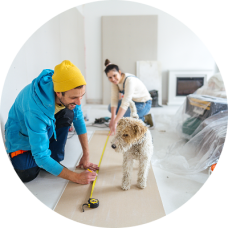 Young couple and their dog working together on a home remodel, measuring and cutting drywall with tools, preparing to install plasterboard—consider using a Civic HELOC for your next home project.