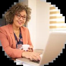 Older woman working at a desk, looking at her laptop while reviewing her retirement accounts.