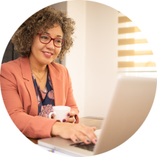Older woman working at a desk, looking at her laptop while reviewing her retirement accounts.