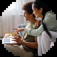 Couple sitting together on a couch, browsing cars on a laptop while shopping online for their next vehicle.