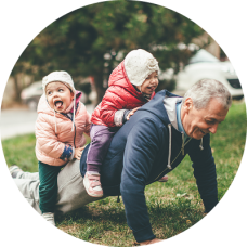 A grandfather doing a push-up with two small children laughing on his back, symbolizing strength and legacy; conceptually tied to the idea of protecting family wealth through an irrevocable trust.