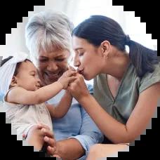 A mother kisses her baby’s hand while sitting on her grandmother’s lap, symbolizing generations—reminder to update your account beneficiaries.