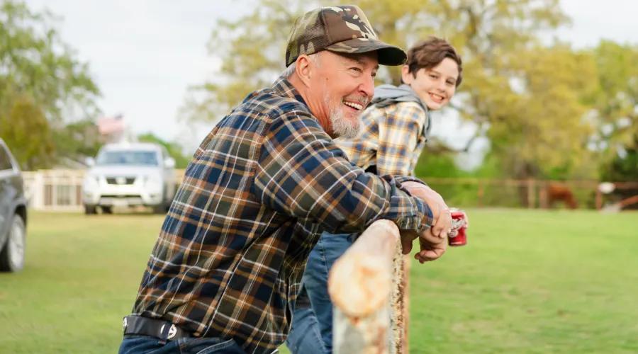 Grandfather and grandson looking over a field from a wooden fence.
