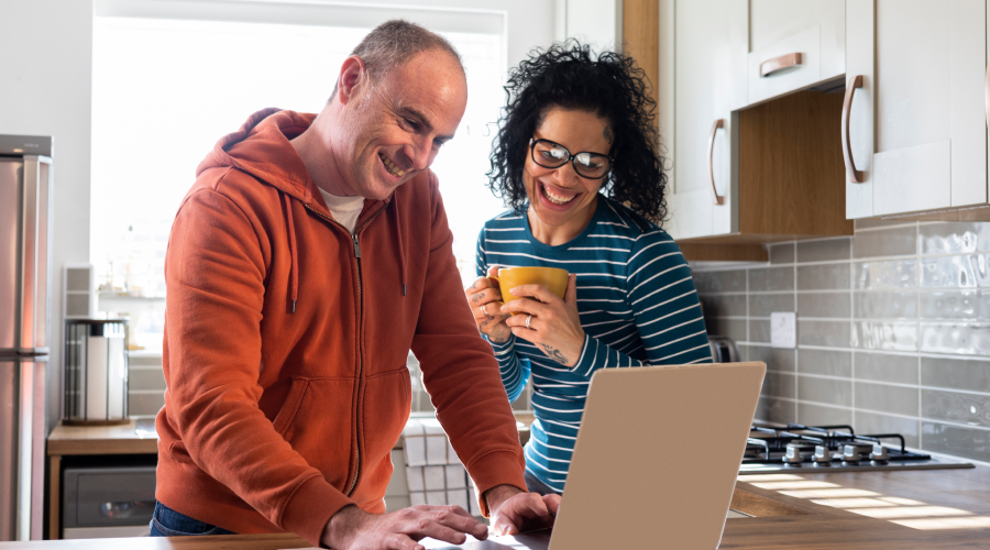 Couple at the kitchen counter, enjoying there morning coffee while opening a Civic Essential Checking Account on a laptop.