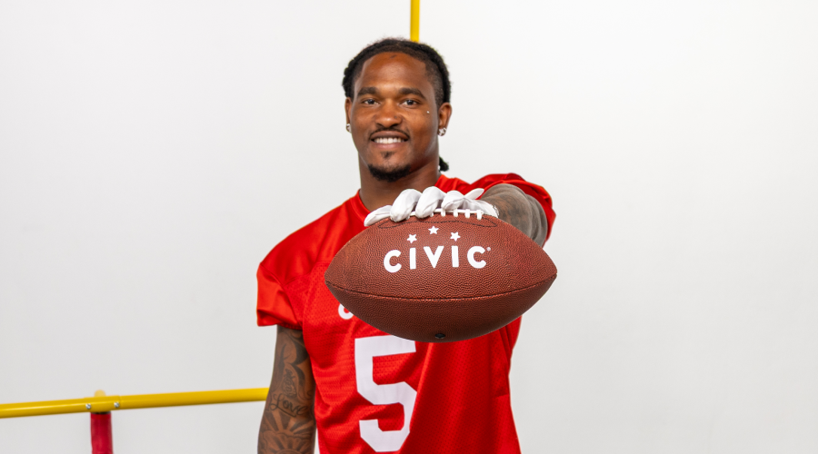 Rico Dowdle holding a football with the Civic logo. 