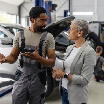 Mechanic in a garage with client discussing underlying car issues. 