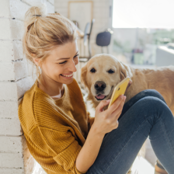 A woman sits on the floor with her dog by her side, checking the growth of her Civic Choice Certificate account on her phone.