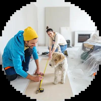 Young couple and their dog working together on a home remodel, measuring and cutting drywall with tools, preparing to install plasterboard—consider using a Civic HELOC for your next home project.