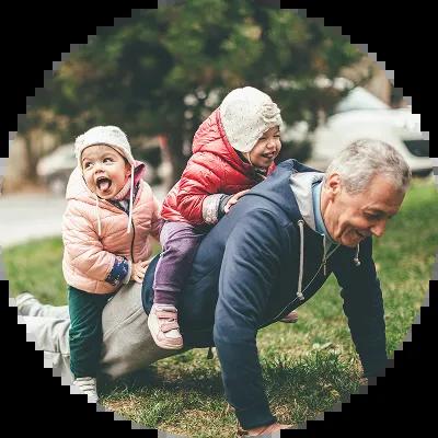 A grandfather doing a push-up with two small children laughing on his back, symbolizing strength and legacy; conceptually tied to the idea of protecting family wealth through an irrevocable trust.