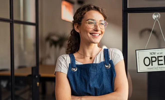 Smiling small business owner showing open sign in her new shop purchased with Civic Business Real Estate Loan.
