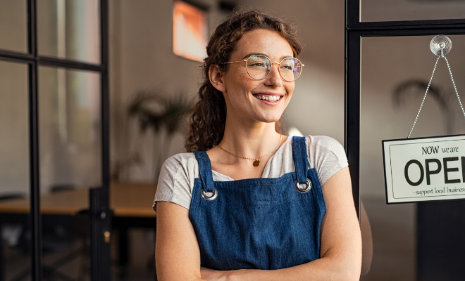 Smiling small business owner showing open sign in her new shop purchased with Civic Business Real Estate Loan.