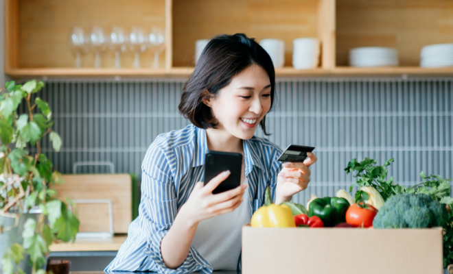 Smiling young Asian woman shopping online with her Civic Business Rewards Credit Card.