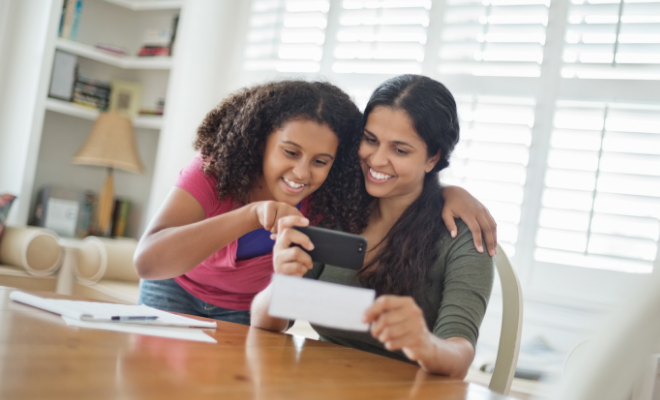 Teen daughter using remote deposit capture to deposit a check with her mother's help.