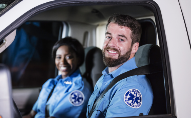 Two paramedics in the front of an ambulance smiling.