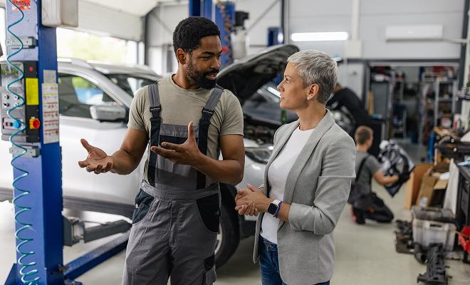 Mechanic in a garage with client discussing underlying car issues. 