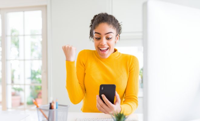 A happy woman smiles as she checks her improved credit score on her cellphone, all thanks to choosing a Civic Credit Builder Loan.
