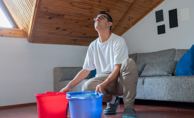 A man holds buckets to catch water leaking from his roof, knowing he can turn to the Civic Emergency Loan for help with repairs.