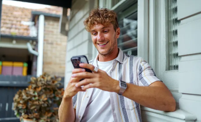 Man on his phone checking the balance of his Civic Essential Checking account while sitting on the front porch. 