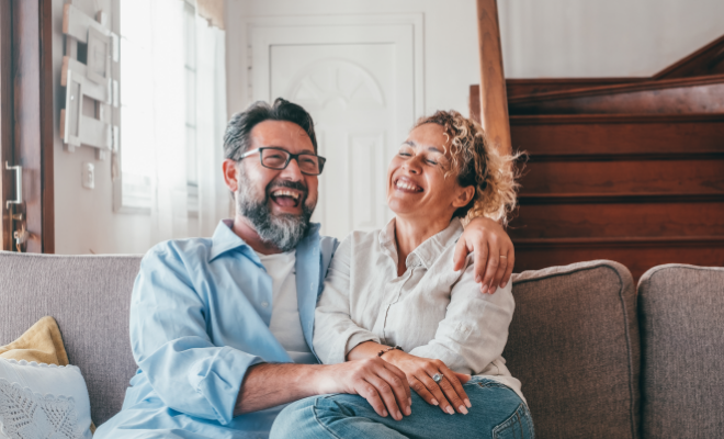 A joyful couple sitting on the sofa, thrilled about their upcoming vacation plans, made possible by their Civic Steady Save Savings Account.