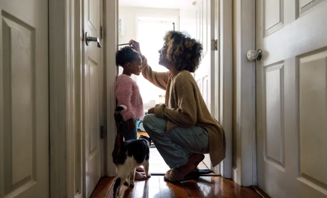 Mother measuring daughter's height and marking on wall at home.