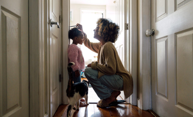 Mother measuring daughter's height and marking on wall at home.