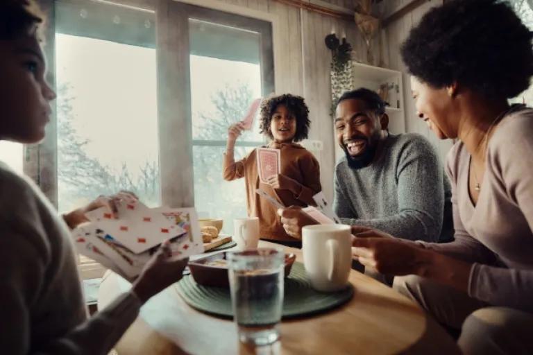 Happy African American family playing cards at home after a day of holiday shopping with the Civic Classic Credit Card.
