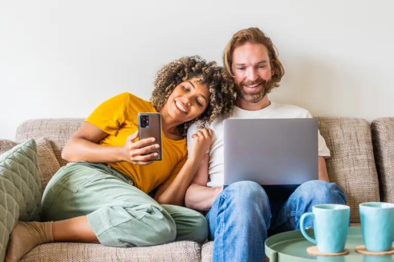 Couple cuddling on the couch looking at there Civic Choice Money Market account through online banking app. 