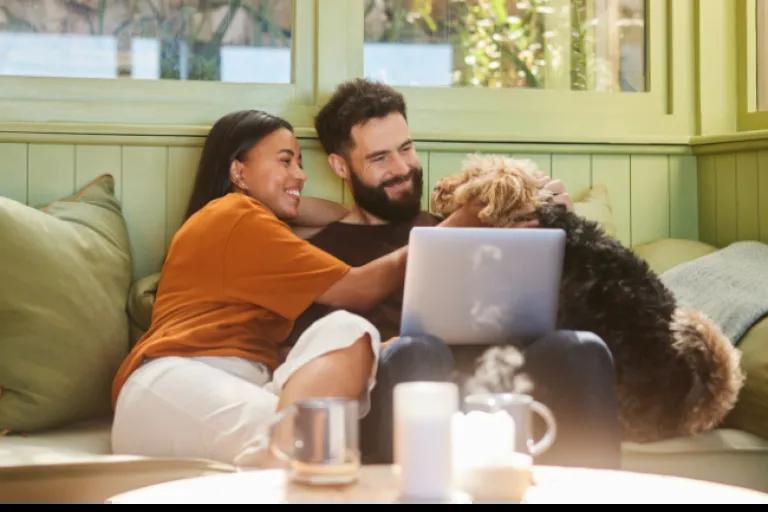 Couple sitting on the sofa with their dog, reading about credit insurance on their laptop via the Civic website.