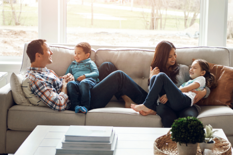 A joyful family cuddles and laughs together on the couch during a peaceful weekend at home, feeling secure and connected after protecting their home with mortgage insurance from Civic’s partner, TruStage.