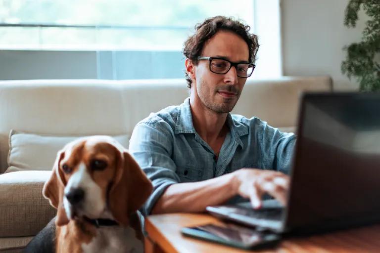 Man checking is Civic accounts on his laptop while sitting on the floor with his Beagle dog by his side