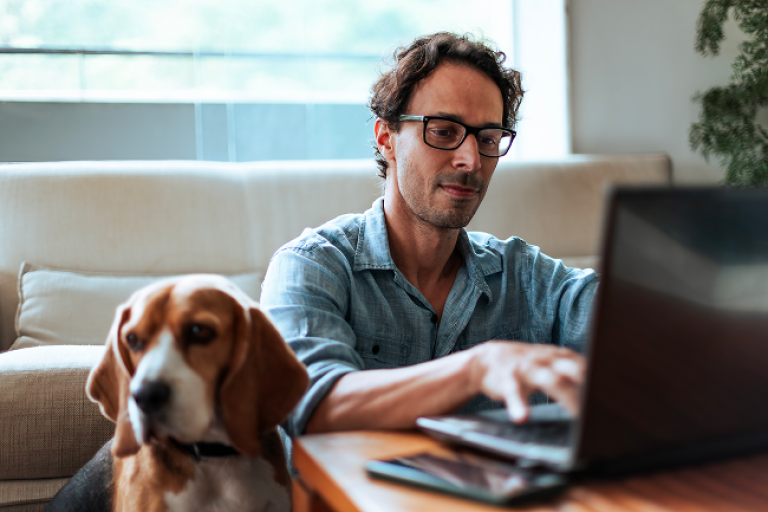 Man checking is Civic accounts on his laptop while sitting on the floor with his Beagle dog by his side