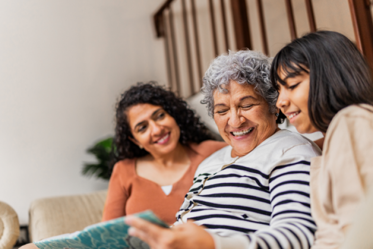 Three generations of women sitting on the sofa, looking at a family photo album.
