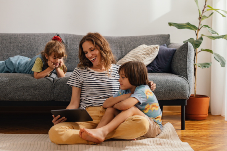  mom sitting on the floor with an iPad, checking her Civic Traditional IRA account, while her two young kids play around her.